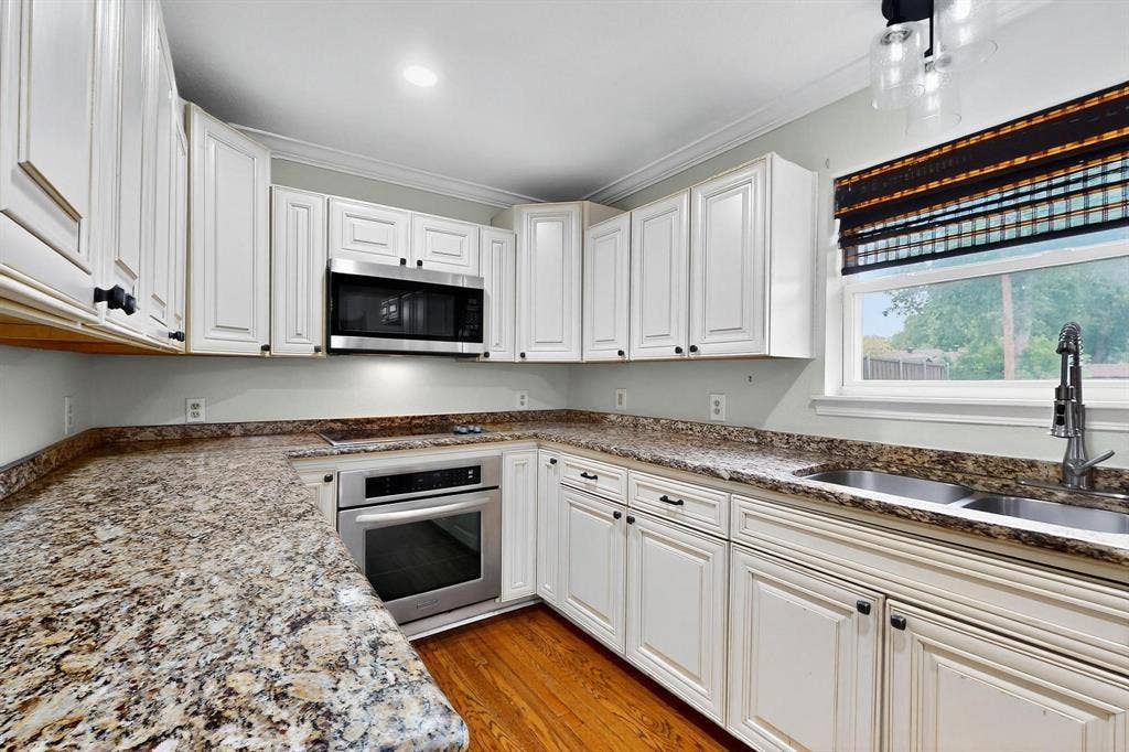 2927 Selma Lane, Farmers Branch, TX 75234 Kitchen with appliances with stainless steel finishes, ornamental molding, white cabinetry, light wood-type flooring, and stone counters