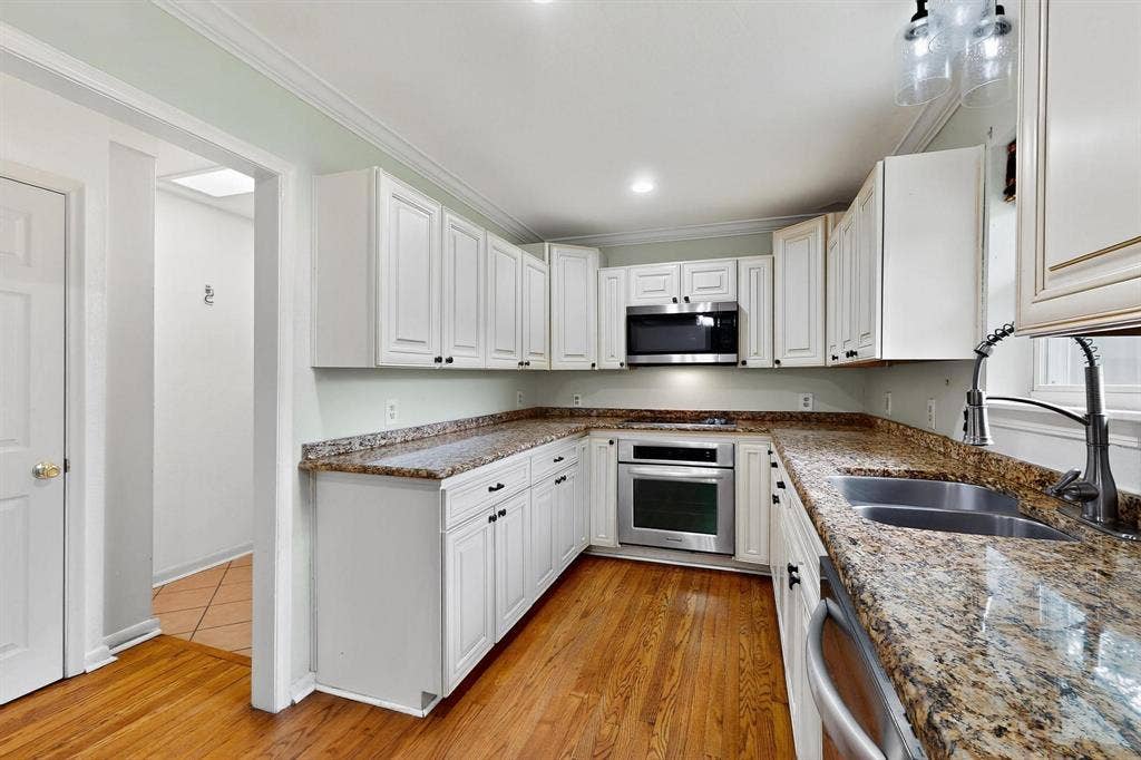 2927 Selma Lane, Farmers Branch, TX 75234 Kitchen with appliances with stainless steel finishes, white cabinetry, crown molding, stone counters, and light wood-style floors
