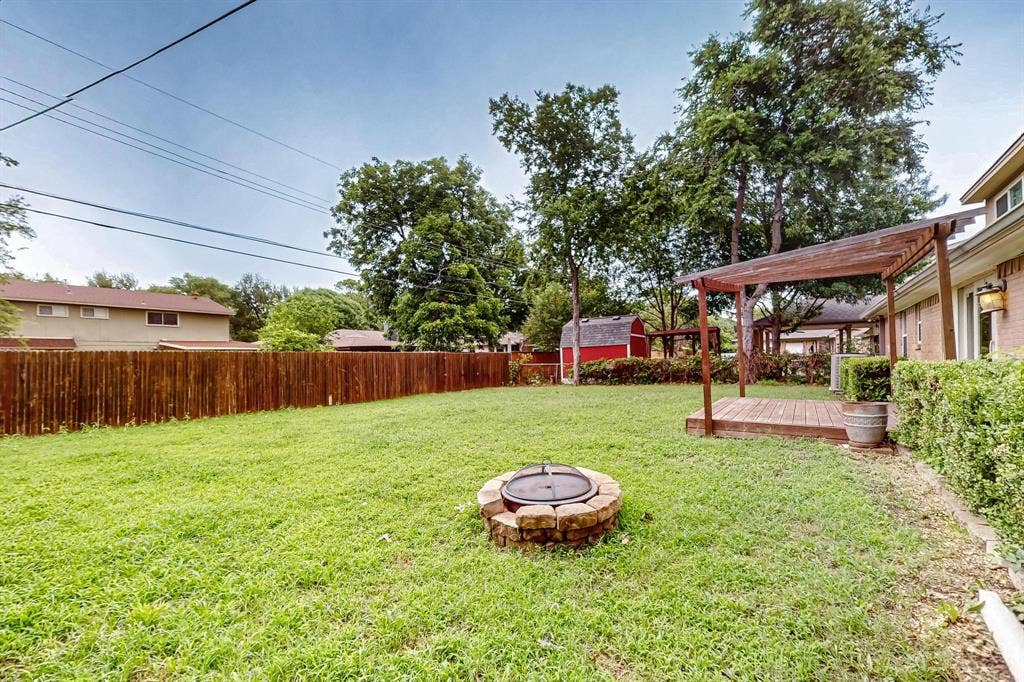 2927 Selma Lane, Farmers Branch, TX 75234 Fenced backyard with a fire pit, a wooden deck, and a storage unit