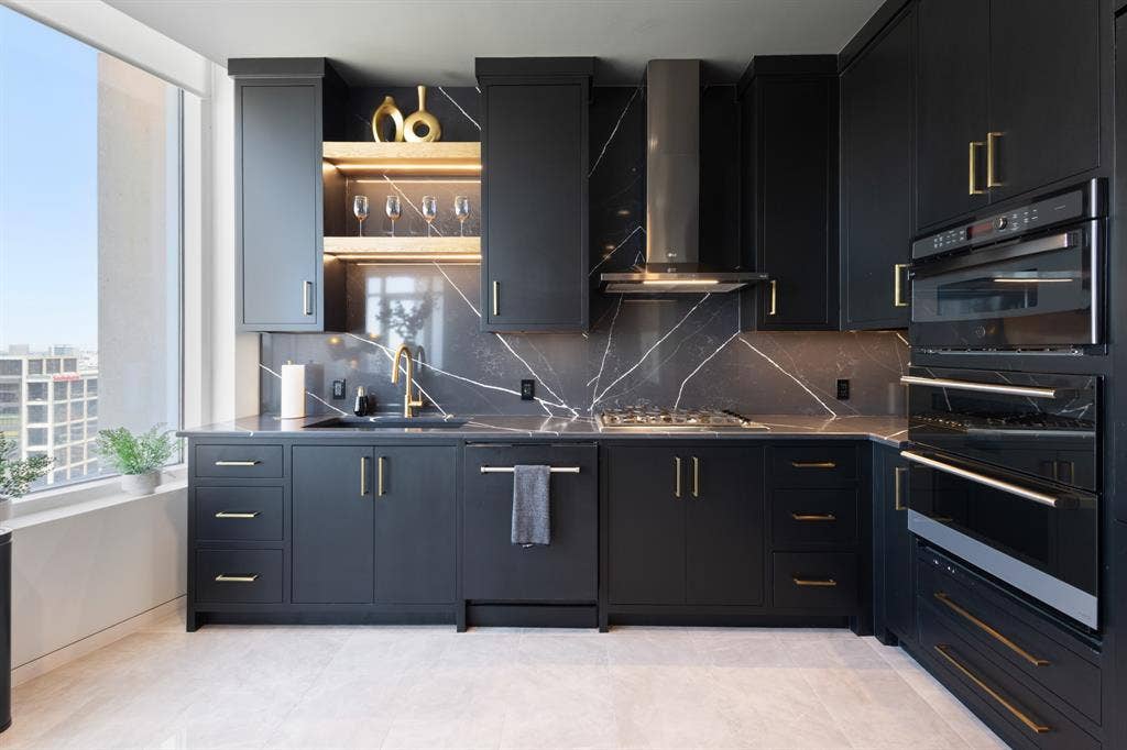 2430 Victory Park Lane, #2401, Dallas, TX 75219 Modern kitchen featuring black cabinetry with gold-tone hardware, a dark marble-patterned backsplash, and a built-in oven and microwave