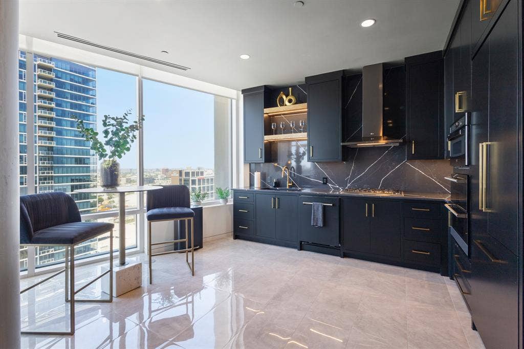 2430 Victory Park Lane, #2401, Dallas, TX 75219 Sleek kitchen featuring dark cabinetry, integrated appliances, gold-finish hardware, a full-height backsplash with veining, and a gas cooktop