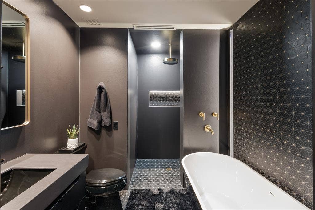 2430 Victory Park Lane, #2401, Dallas, TX 75219 Freestanding soaking tub with brass fixtures, a geometric patterned accent wall, and a large walk-in shower with a rainfall showerhead