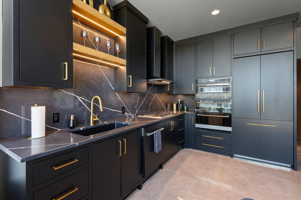 2430 Victory Park Lane, #2401, Dallas, TX 75219 Sleek kitchen featuring dark cabinetry, gold-tone hardware, integrated appliances, and a dramatic veined countertop and backsplash
