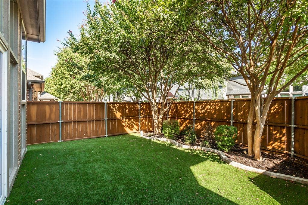 844 Veneto Drive, Allen, TX 75013 Artificial turf backyard with no mowing required, a stained cedar privacy fence on steel posts, andmature crape myrtles. Stone-edged planting bed with shrubs along the fence line.