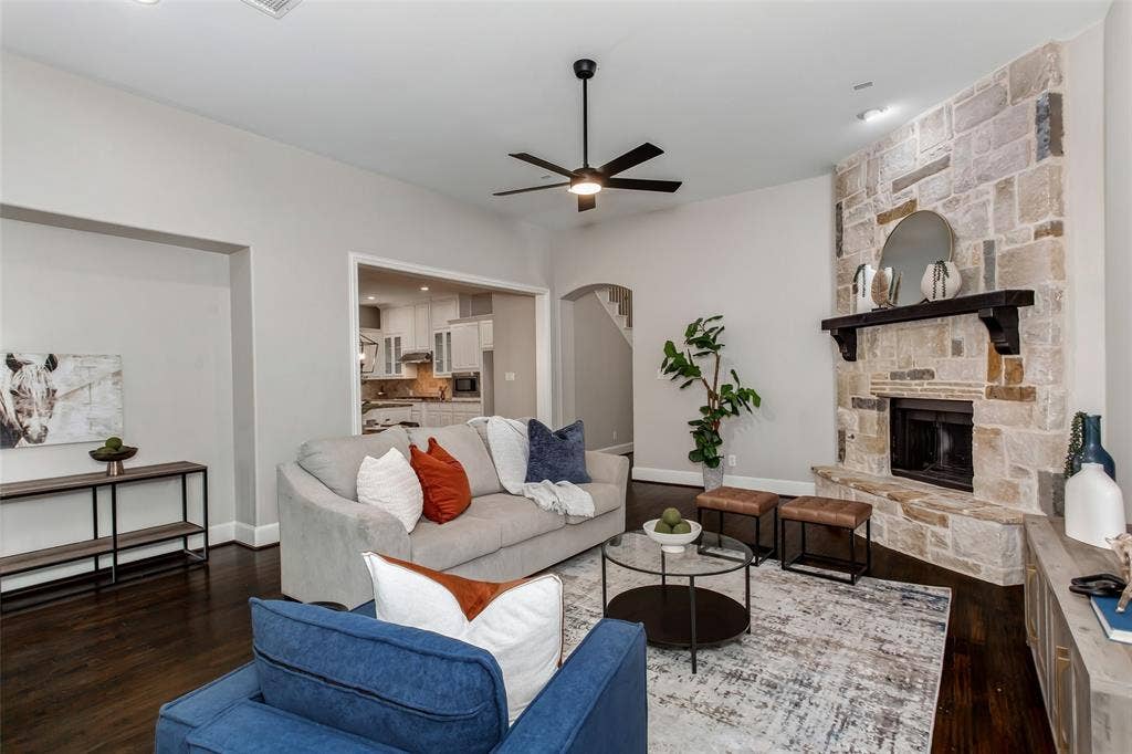 844 Veneto Drive, Allen, TX 75013 Stone-clad fireplace with dark wood mantel, dark wood-finish flooring, ceiling fan with integrated lighting, and arched entryways