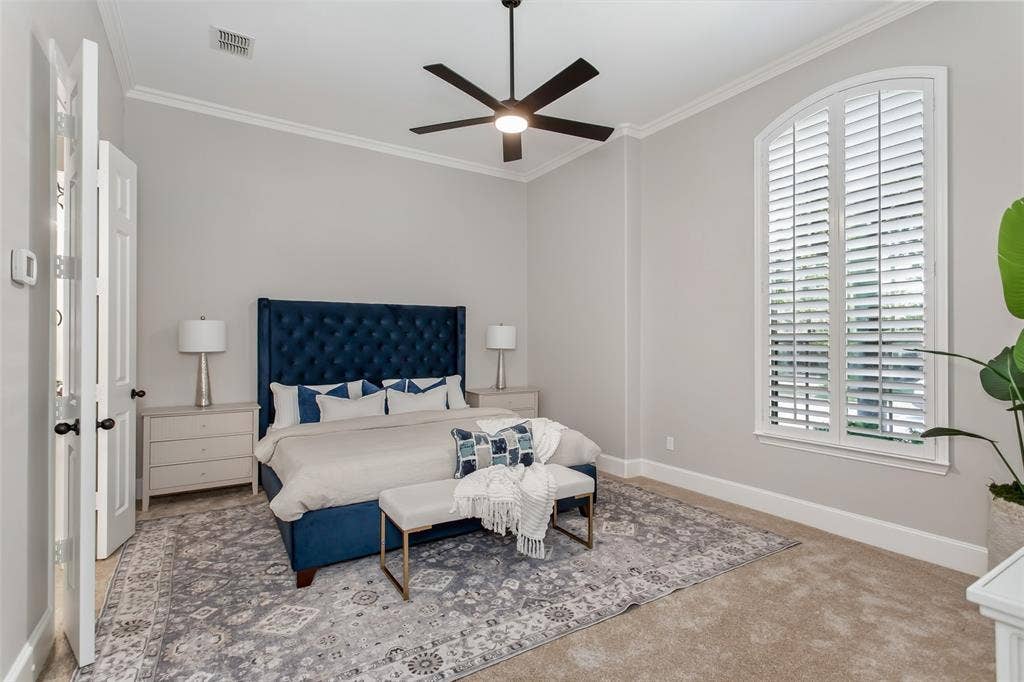 844 Veneto Drive, Allen, TX 75013 Downstairs primary bedroom with crown molding, an arched window with plantation shutters, and new2026 carpet. New ceiling fan with an LED light.