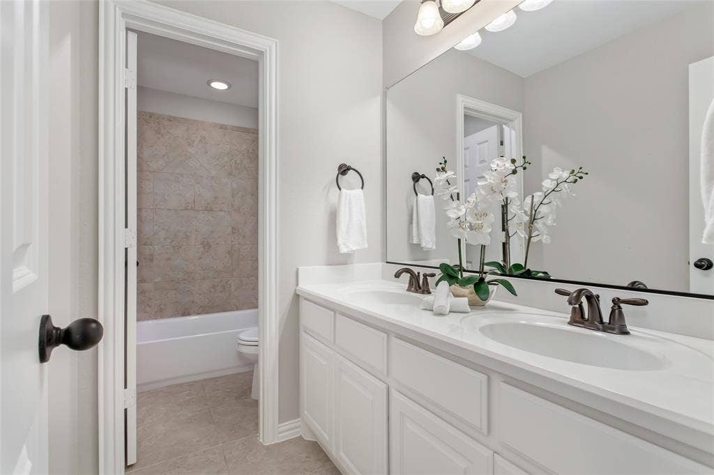 844 Veneto Drive, Allen, TX 75013 Dual-sink vanity with white cabinetry and oil-rubbed bronze faucets. A separate room holds the tub andshower combination and toilet.