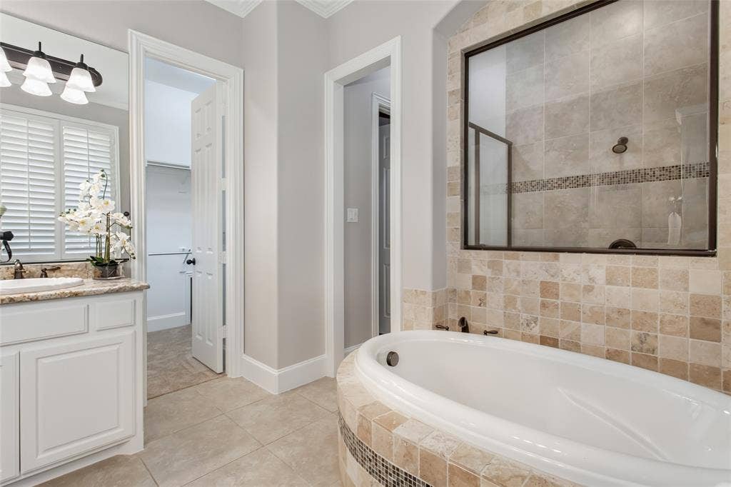 844 Veneto Drive, Allen, TX 75013 Walk-in shower with travertine tile, a glass mosaic accent band, and oil-rubbed bronze fixtures besidethe garden tub. Doorway to the walk-in closet on the left.
