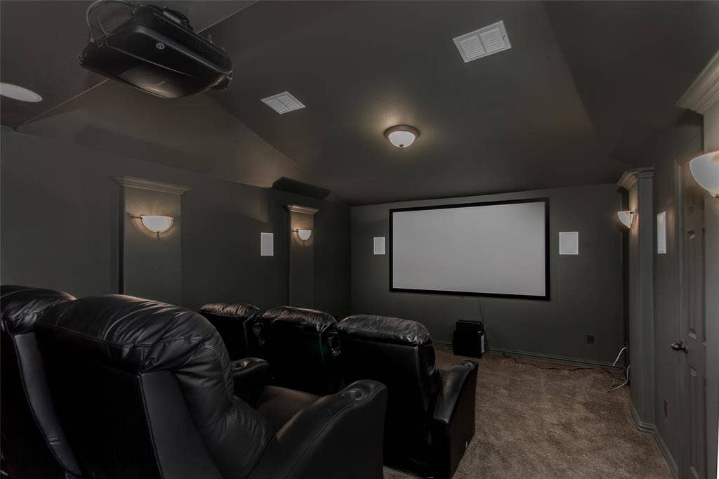 844 Veneto Drive, Allen, TX 75013 Dedicated media room with a projection screen, ceiling-mounted projector, in-wall speakers, and wallsconces. Dark walls and carpet for a theater setting.