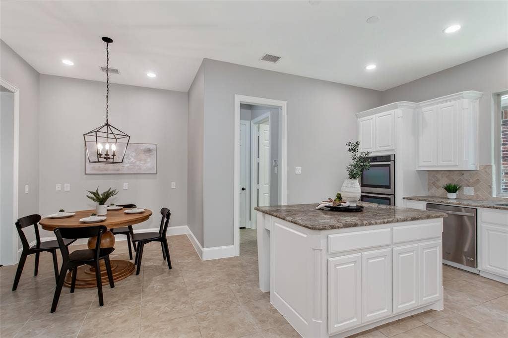 844 Veneto Drive, Allen, TX 75013 Granite island with cabinet storage sits between the kitchen and a breakfast nook lit by a new 2026lantern pendant. Tile flooring runs through both spaces, with recessed lighting overhead.