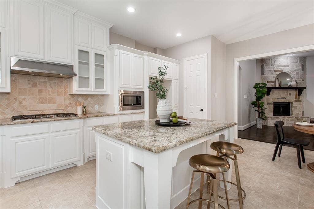 844 Veneto Drive, Allen, TX 75013 Granite island with bar seating looks across the breakfast area to the stone fireplace in the family room.Stainless vent hood, built-in microwave, and pantry door on the back wall.