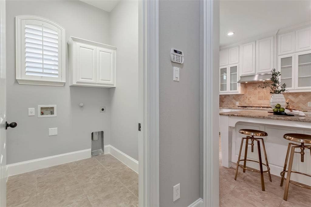 844 Veneto Drive, Allen, TX 75013 Utility room off the kitchen with tile flooring, an upper storage cabinet, and an arched window withplantation shutters. Washer and dryer connections on the back wall.