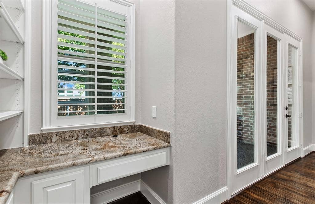 844 Veneto Drive, Allen, TX 75013 The family room flows to a built-in home management area with open shelving, a granite counter, andcabinet storage. French doors on the right open to the enclosed sunroom.
