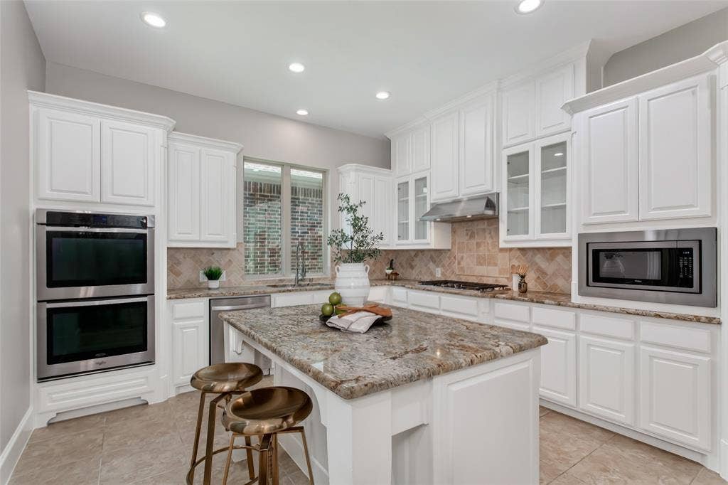 844 Veneto Drive, Allen, TX 75013 White cabinetry with glass-front uppers, granite countertops, and a tumbled stone herringbonebacksplash. Stainless double wall ovens, 5-burner gas cooktop with vent hood, built-in microwave,dishwasher, and a center island with seating.