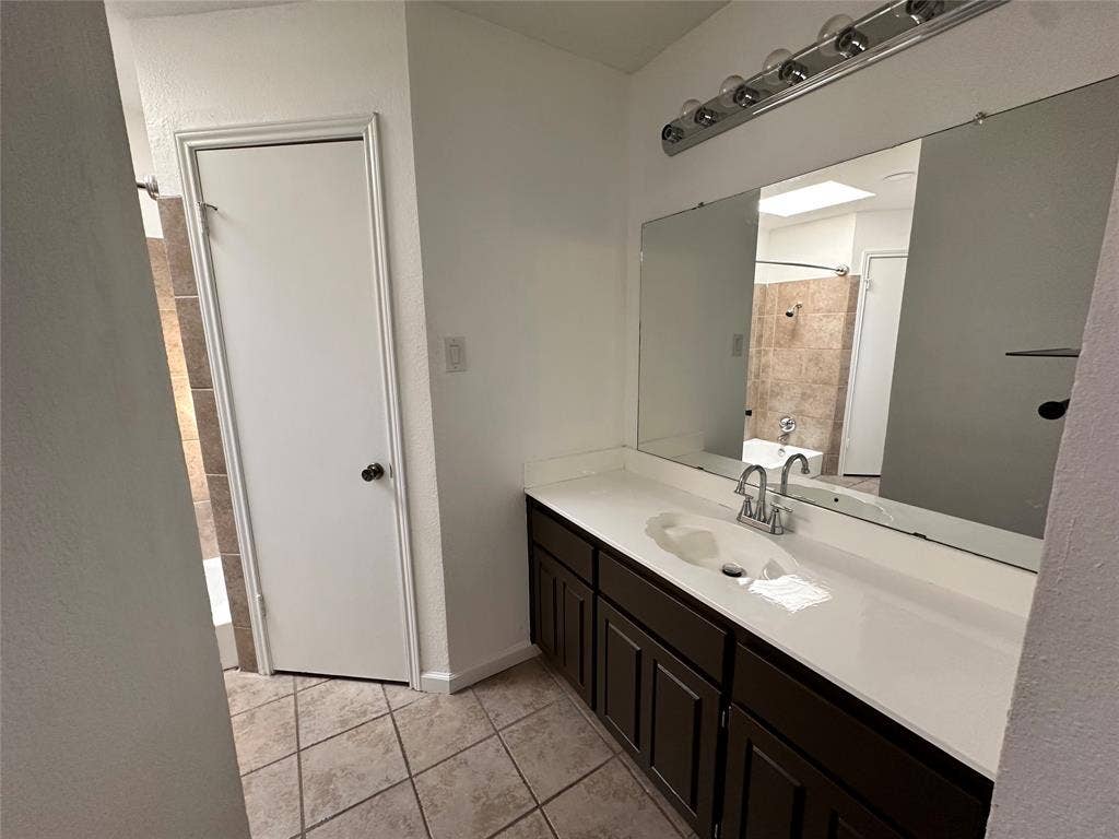 Vanity with an integrated sink, wall to wall mirror, ample counter and storage space, and a chrome light fixture