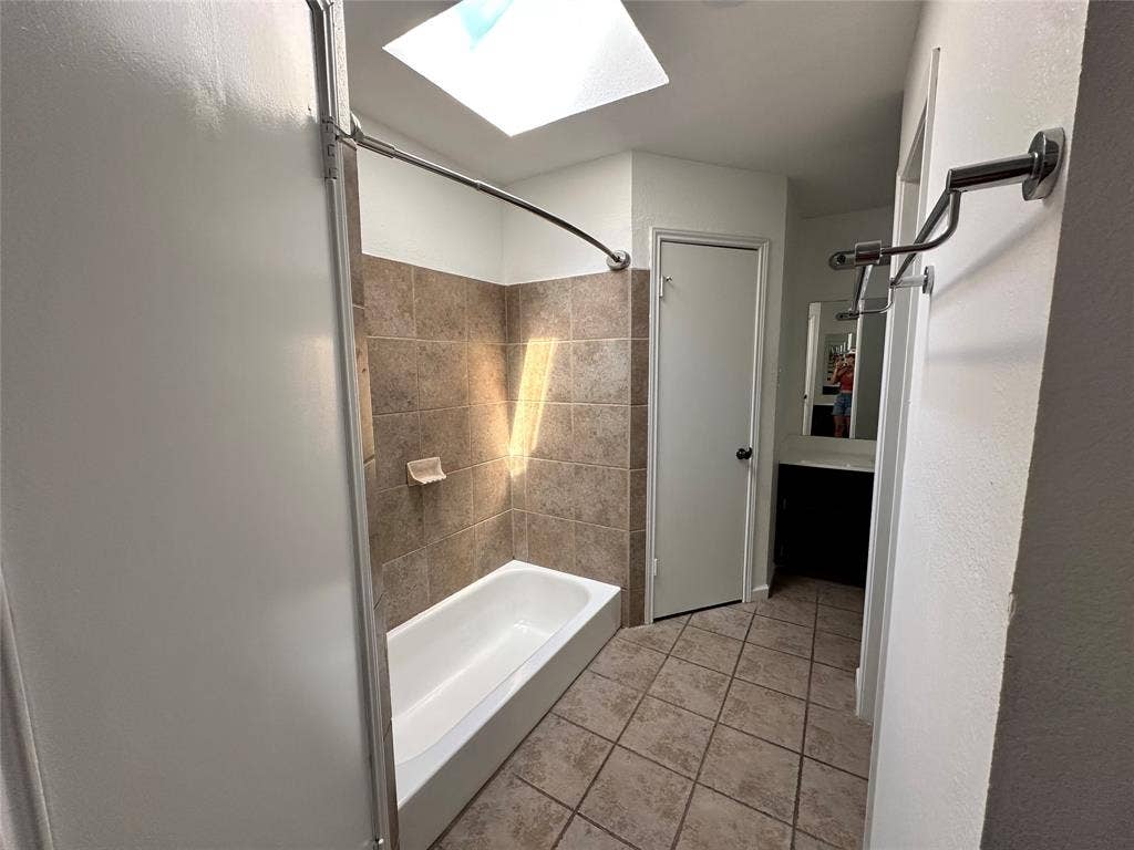 Bathroom featuring a skylight, tile flooring, a built-in bathtub with tile surround, a dark wood-finish vanity, and a wall-mounted mirror