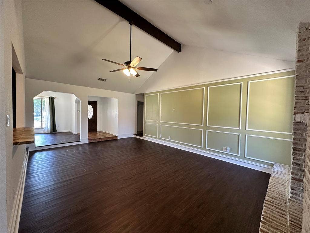 Vaulted ceiling with exposed wood beam, wood-finish flooring, accent wall with decorative molding, and brick column