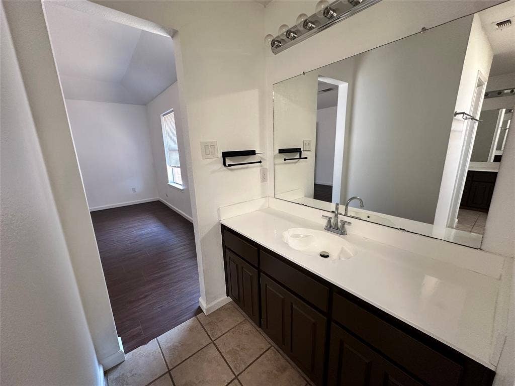White vanity with integrated sink, chrome faucet, and expansive mirror with overhead lighting