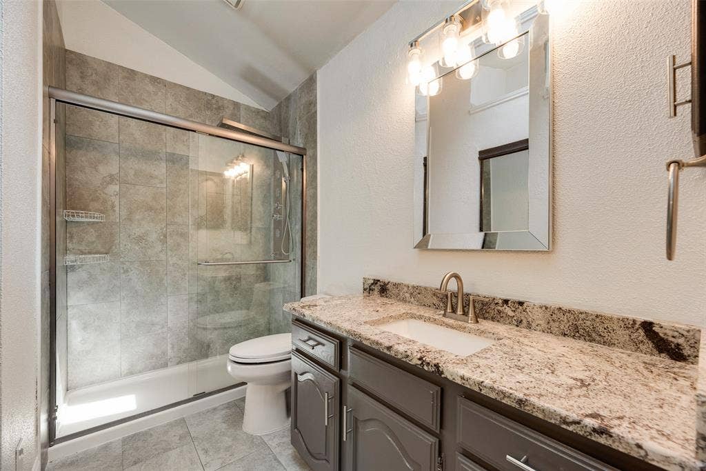 17490 Meandering Way, #202, Dallas, TX 75252 Walk-in shower with tiled surround and glass enclosure, white toilet, vanity with undermount sink, granite countertop, and brushed nickel fixtures