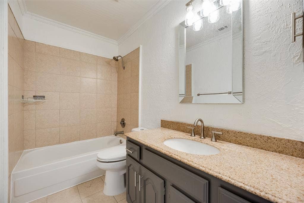 17490 Meandering Way, #202, Dallas, TX 75252 Bathroom featuring a bathtub with tiled surround, a vanity with a light-colored countertop, and a framed mirror with overhead lighting