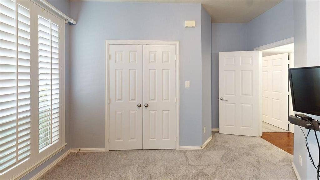 Window with white plantation shutters, light gray wall color, two panel doors, and gray carpet flooring