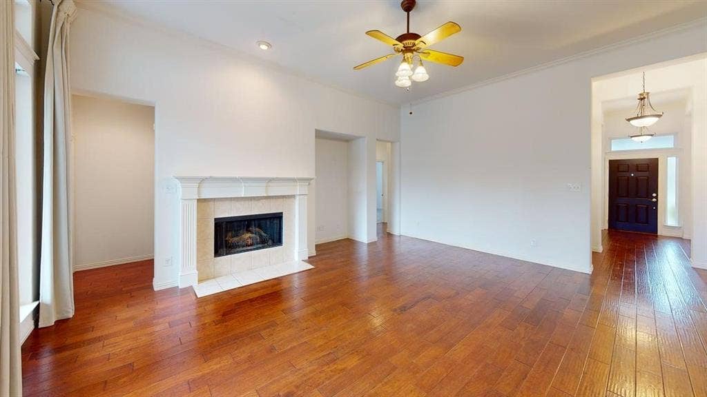 Wood-finish flooring throughout, a stone mantel fireplace with tile surround, a built-in ceiling fan, recessed lighting, and a dark wood entry door with transom and sidelight windows