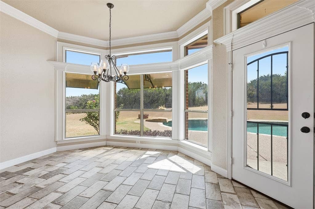 Bay window with multiple large panes, tile flooring, crown molding, and a decorative chandelier