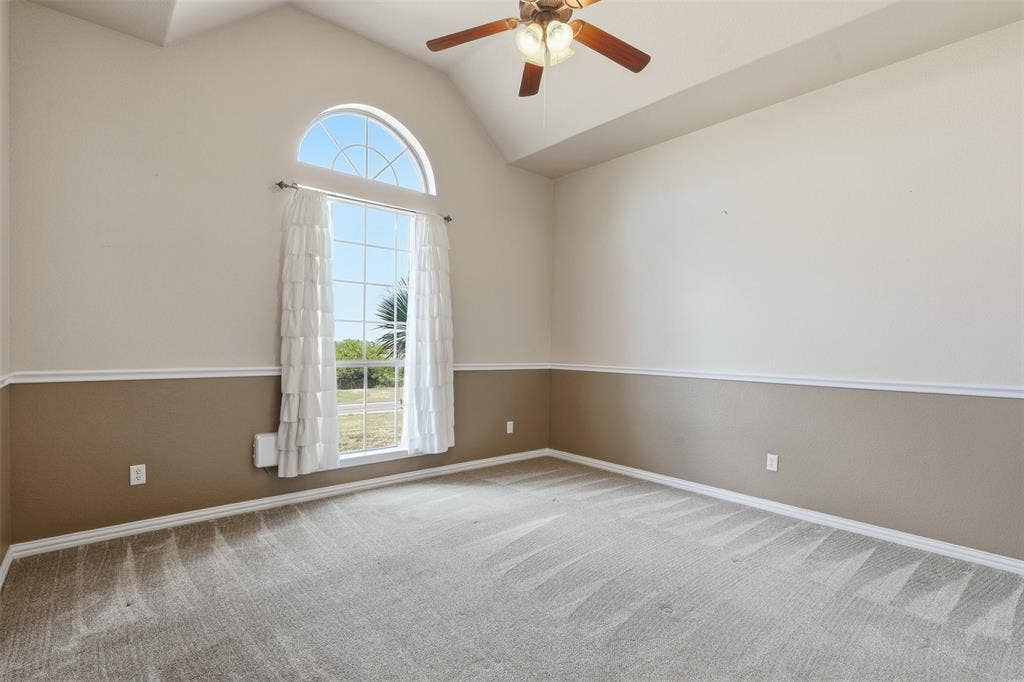 Vaulted ceiling with a ceiling fan, arched transom window, picture window, and chair rail molding