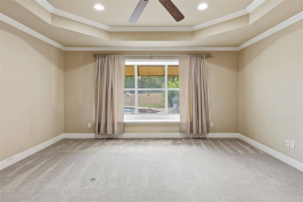 Tray ceiling with crown molding, recessed lighting, ceiling fan, large picture window, and light-toned carpeting