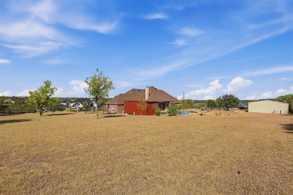 Expansive open yard with a red-sided structure, a light-colored metal outbuilding, and a visible pool area
