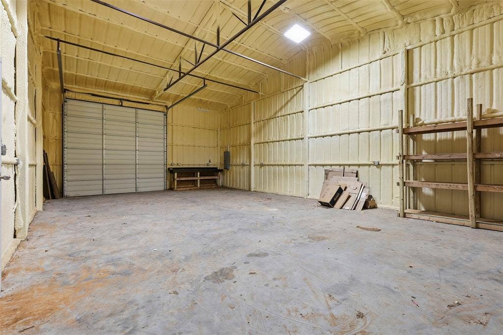 Spacious interior with durable concrete flooring, a large roll-up door, and extensive wall and ceiling insulation