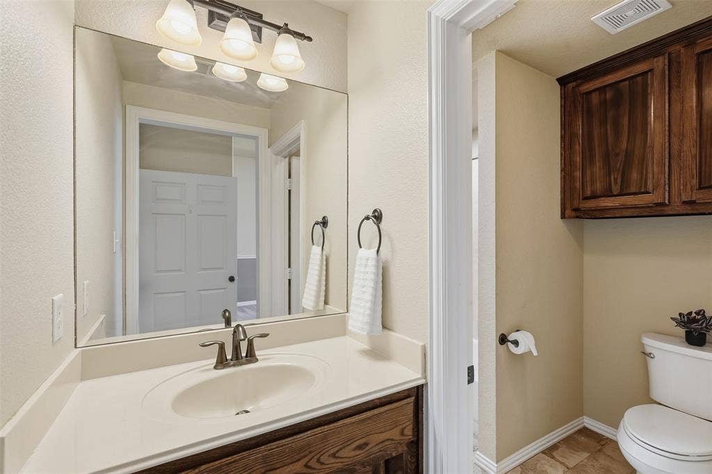 Vanity with an integrated sink and brushed nickel faucet, large wall mirror, and overhead four-light fixture