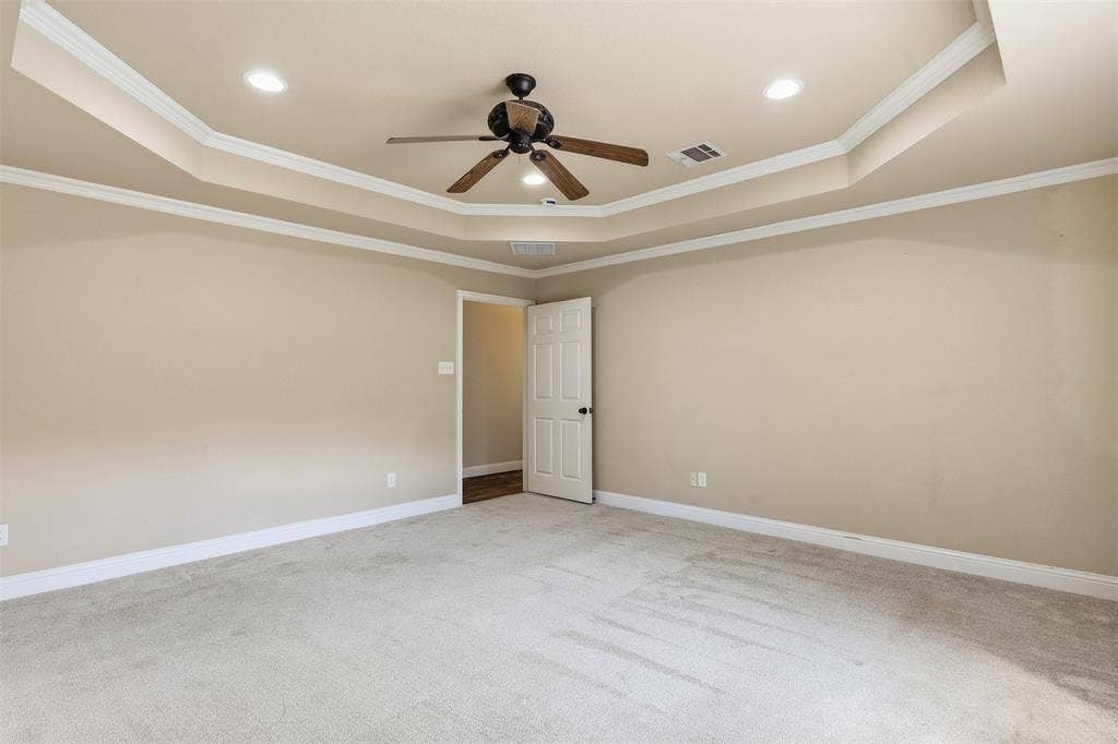 Tray ceiling with recessed lighting and a ceiling fan, light-colored carpet, and an interior door