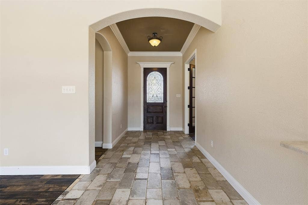 Arched entryways, coffered ceiling, decorative glass front door, rectangular floor tiles, and recessed lighting