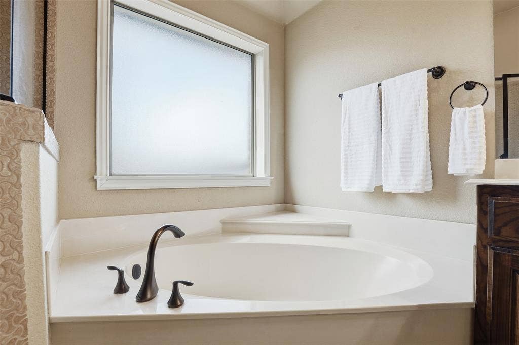 Built-in soaking tub with bronze-finish fixtures, a frosted window, and a surrounding light-toned countertop