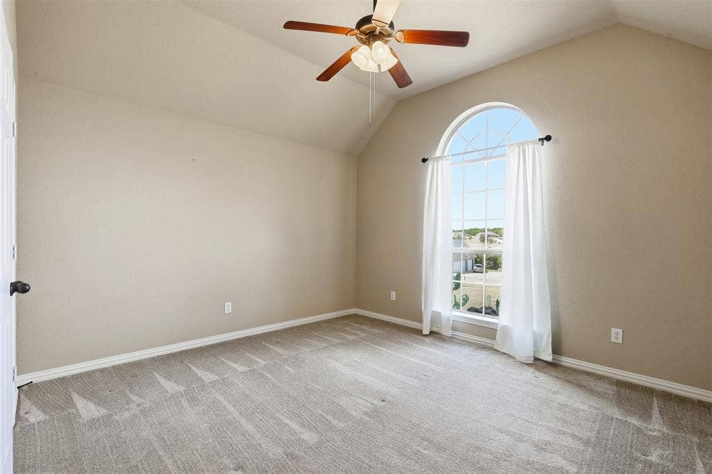 Vaulted ceiling, arched window, carpeted flooring, and a ceiling fan with light fixture
