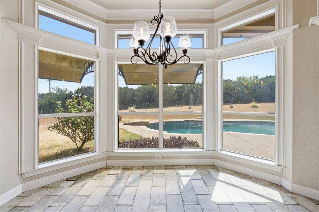 Bay window dining space featuring decorative crown molding, stone tile flooring, and an ornamental chandelier