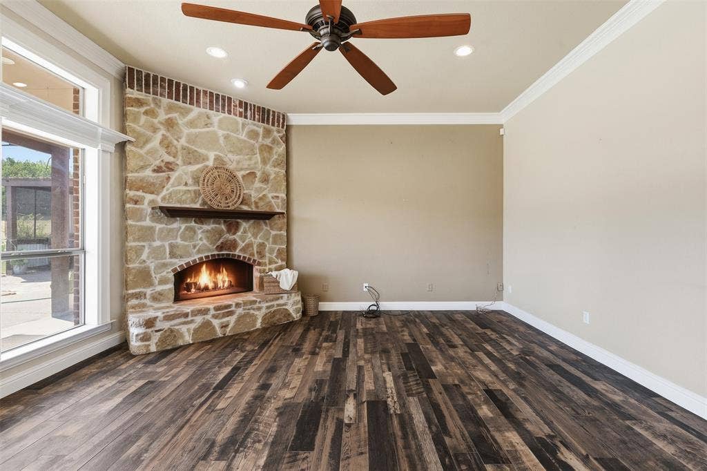 Corner stone fireplace with wood mantel, wood-finish flooring, recessed lighting, and a ceiling fan