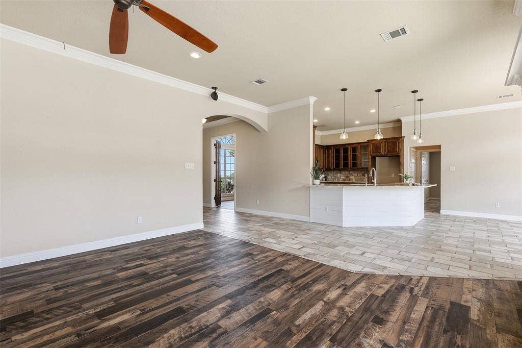 Wood-finish flooring, recessed lighting, ceiling fan with light, crown molding, and an arched doorway