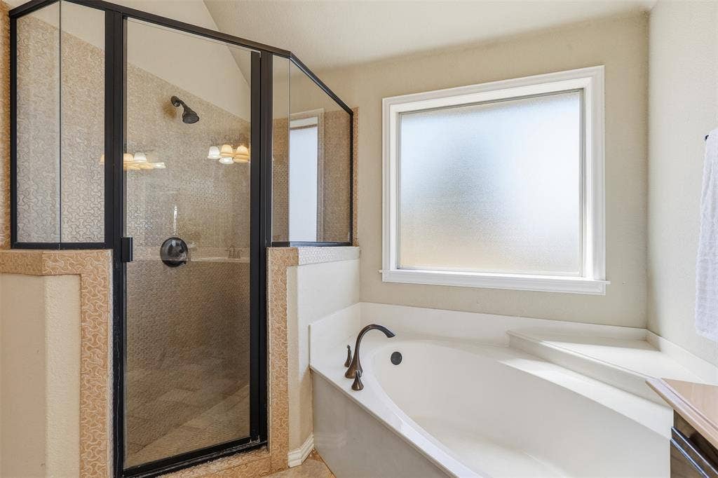 Walk-in shower with dark-framed glass enclosure, tiled walls, and built-in tub with a dark bronze faucet