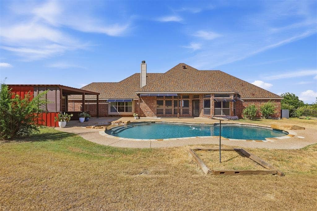 Brick exterior residence featuring a freeform swimming pool, extensive patio decking, a covered outdoor structure, and a red metal shed