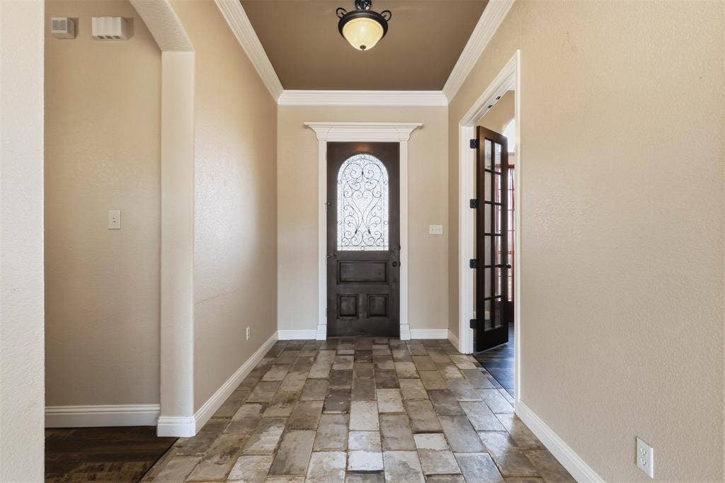 Entryway featuring a decorative dark wood door with wrought iron detailing, large format tile flooring, crown molding, and a tray ceiling with a semi-flush mount light fixture