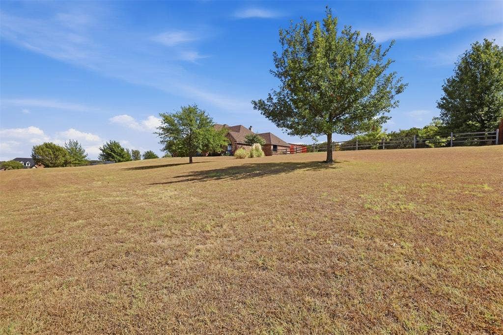 Expansive sloped lawn with scattered mature trees and a distant wood fence