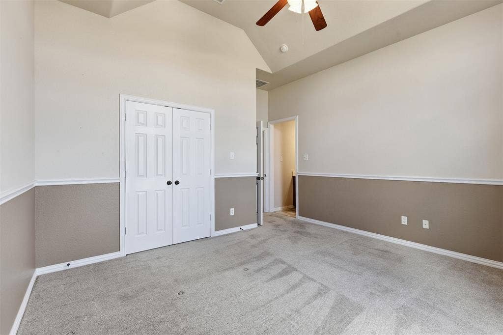 Vaulted ceiling, ceiling fan, bi-fold panel doors, two-tone wall treatment, and light-toned carpeting