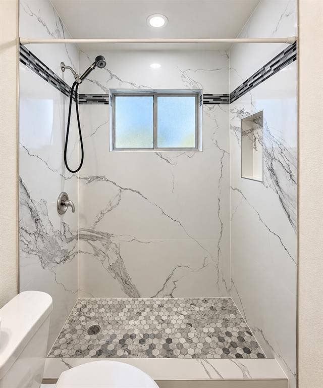 Shower with marble-look tile walls, mosaic hexagon floor, recessed lighting, and an integrated shower niche