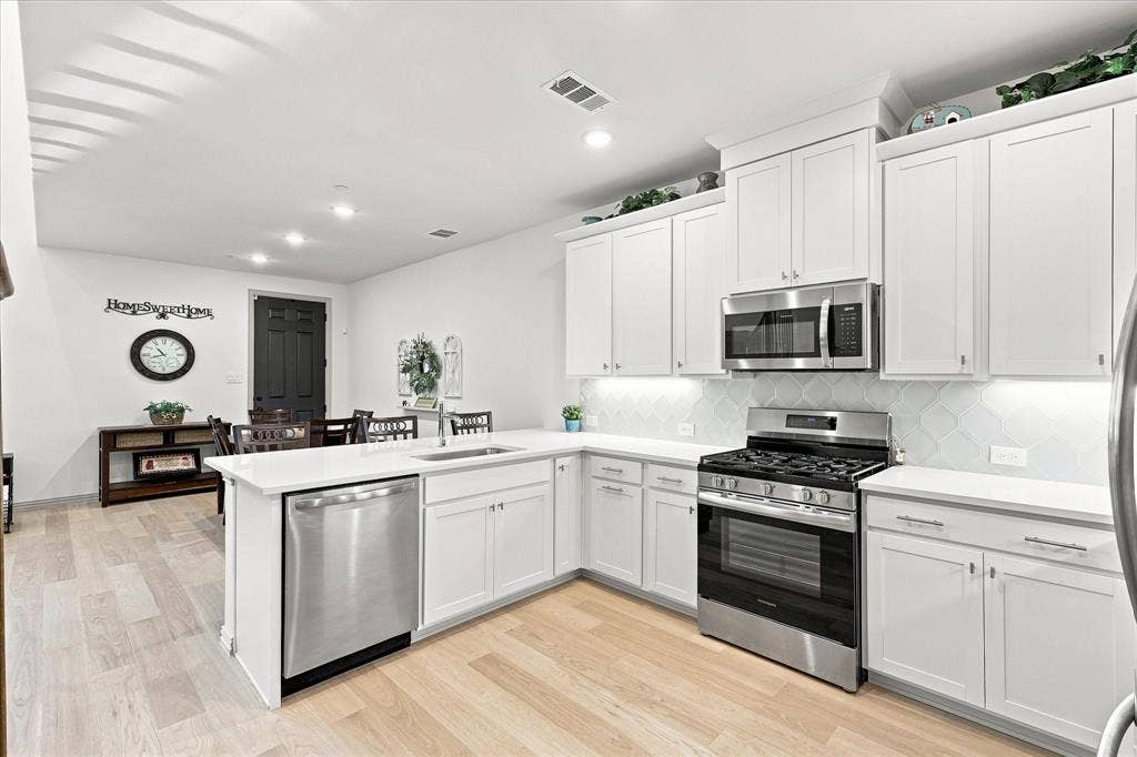 612 4th Street, Argyle, TX 76226 Modern kitchen featuring white cabinetry, stainless steel appliances, light wood-finish flooring, a tile backsplash, and recessed lighting