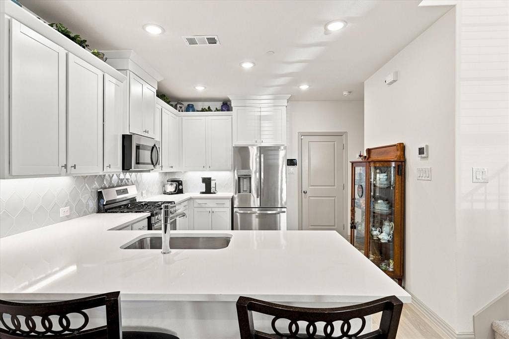 612 4th Street, Argyle, TX 76226 U-shaped kitchen featuring white cabinetry, light-toned countertops, a stainless steel sink with a gooseneck faucet, and integrated stainless steel appliances