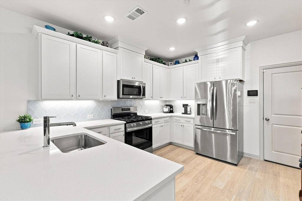 612 4th Street, Argyle, TX 76226 Modern kitchen featuring white cabinetry, white quartz-style countertops, stainless steel appliances, a tile backsplash, and light wood-finish flooring throughout. Under cabinet lighting is a bonus