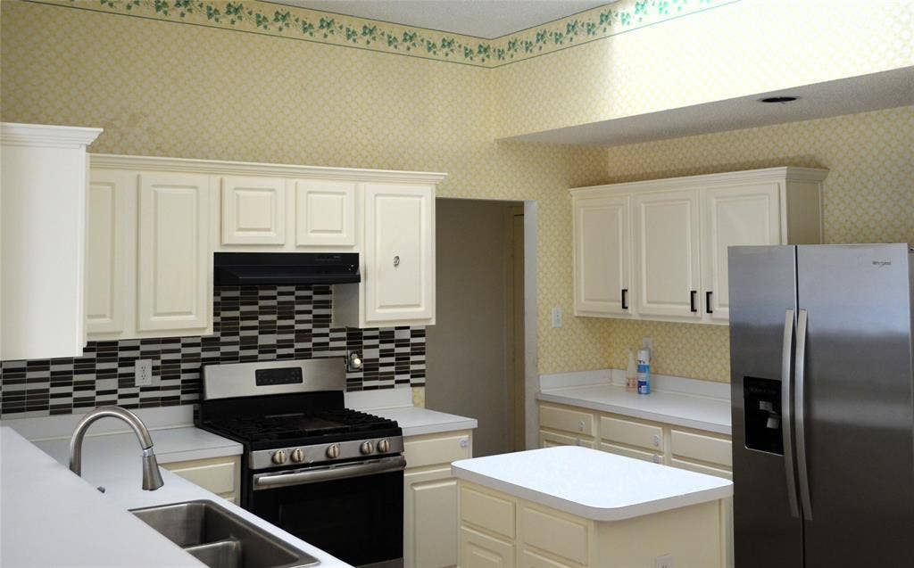 3994 Sword Dancer Way, Grand Prairie, TX 75052 Kitchen featuring white paneled cabinetry, stainless steel appliances, a center island, a black and white mosaic tile backsplash, and a double basin sink with a gooseneck faucet