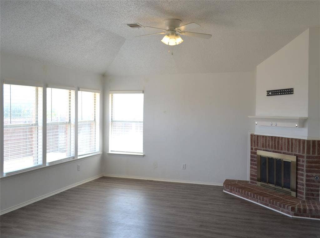 3994 Sword Dancer Way, Grand Prairie, TX 75052 Vaulted ceiling with ceiling fan, multiple windows with blinds, wood-finish flooring, and a brick fireplace with a mantel